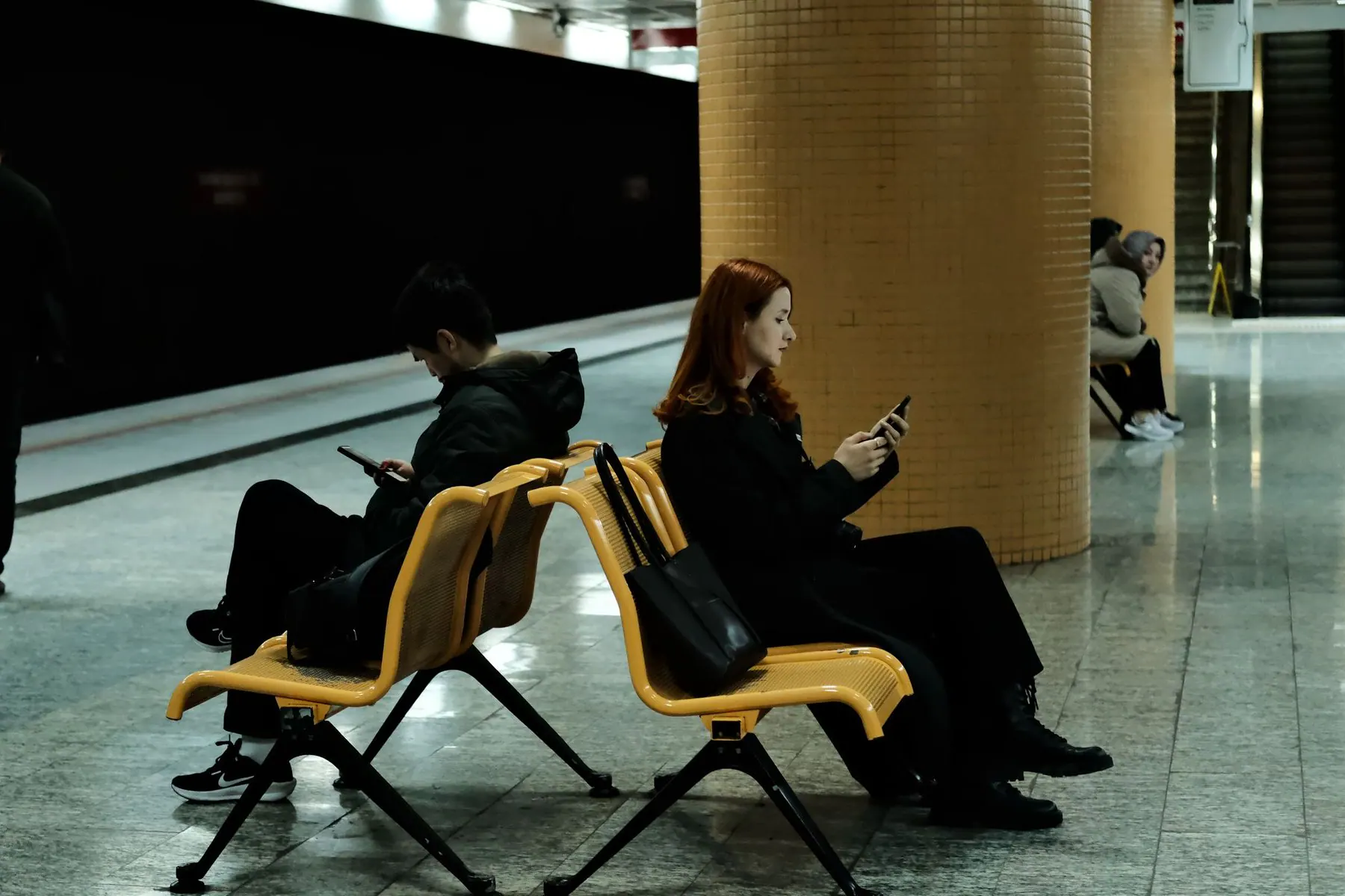 Two travelers checking phones on a metro platform